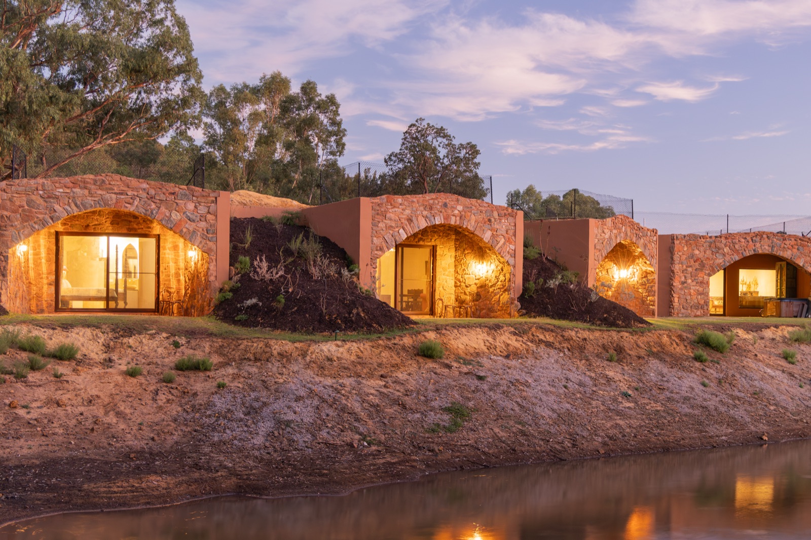 A rammed-earth home beside a dam at dusk